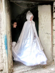 A Palestinian bride in traditional white costume and pointed hood steps out of her house on her wedding day.